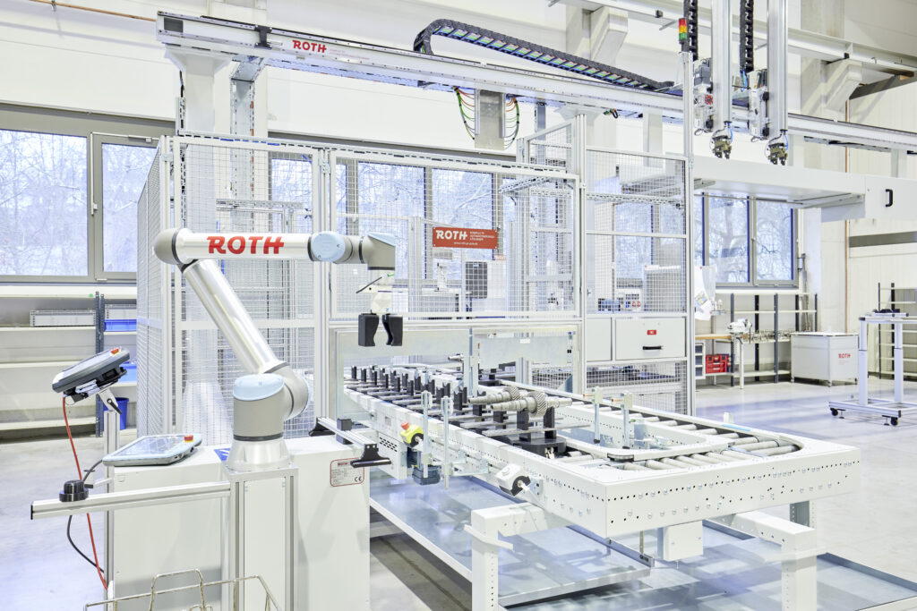 Ein kolaborativer Roboter platziert Werkstücke auf einem Förderband vor einem Schutzzaun in industrieller Umgebung