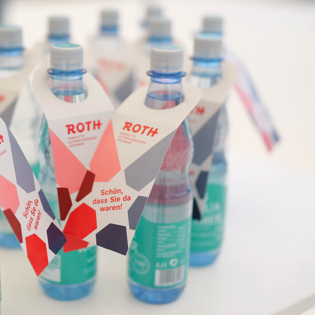 Kleine Wasserflaschen mit Flaschenhalsetikett auf dem ein: "Schön, dass Sie da waren" zu lesen ist.