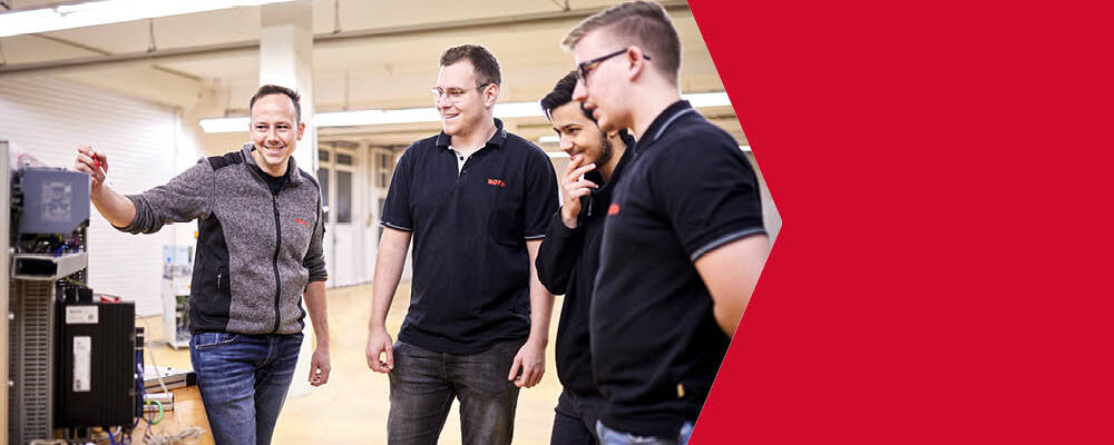 Drei junge Studenten lassen sich von einem weiteren Mann etwas an einer Steuerung erklären