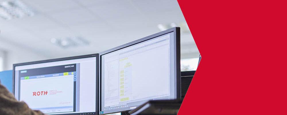 Im Vordergrund stehen zwei große Bildschirme an denen programmiert wird