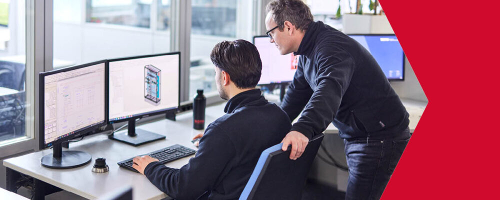 Zwei Mitarbeiter besprechen Arbeitsergebnisse an einem Dual-Monitor-Arbeitsplatz.